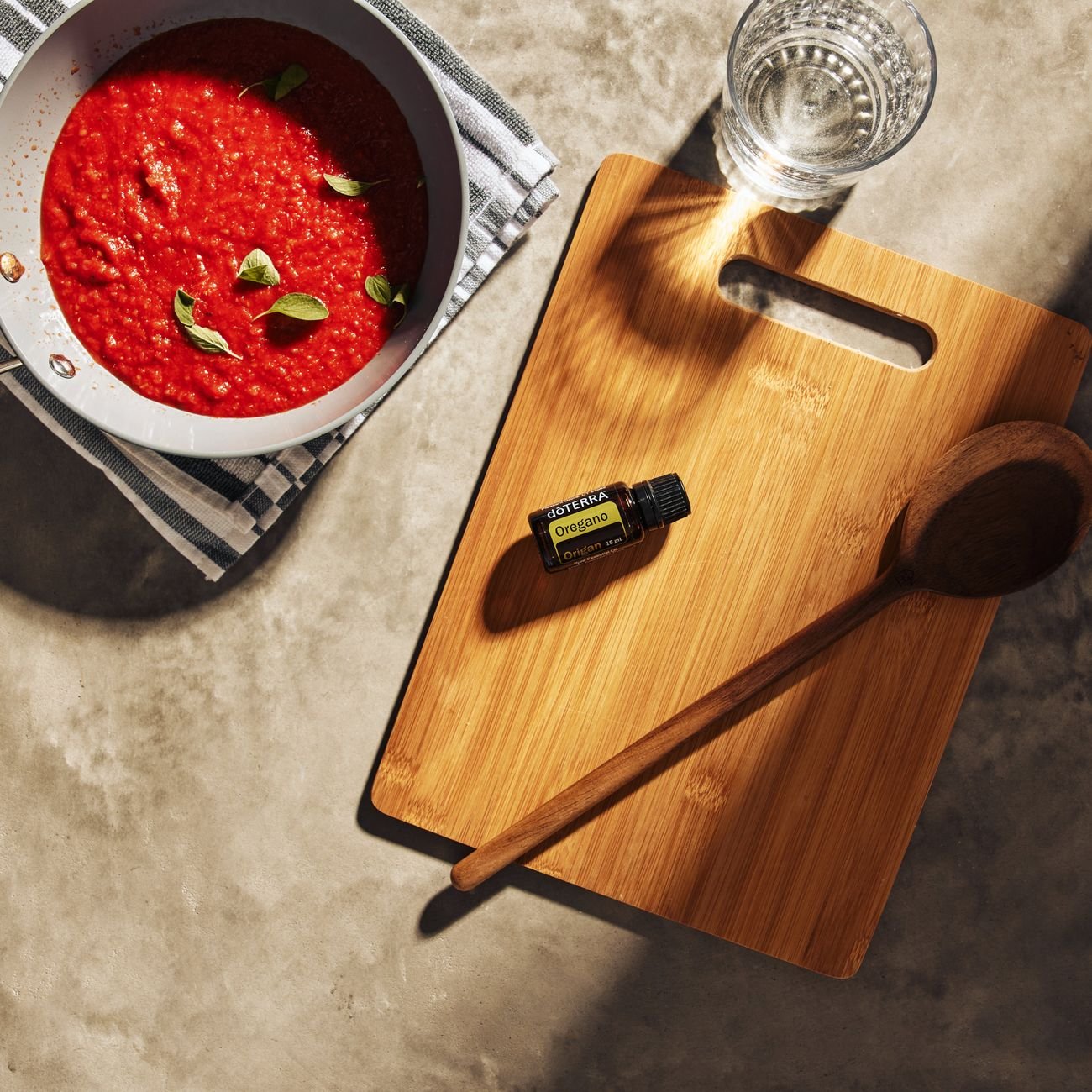 Flat lay of tomato sauce with oregano, wooden cutting board, and glass of water in a kitchen.