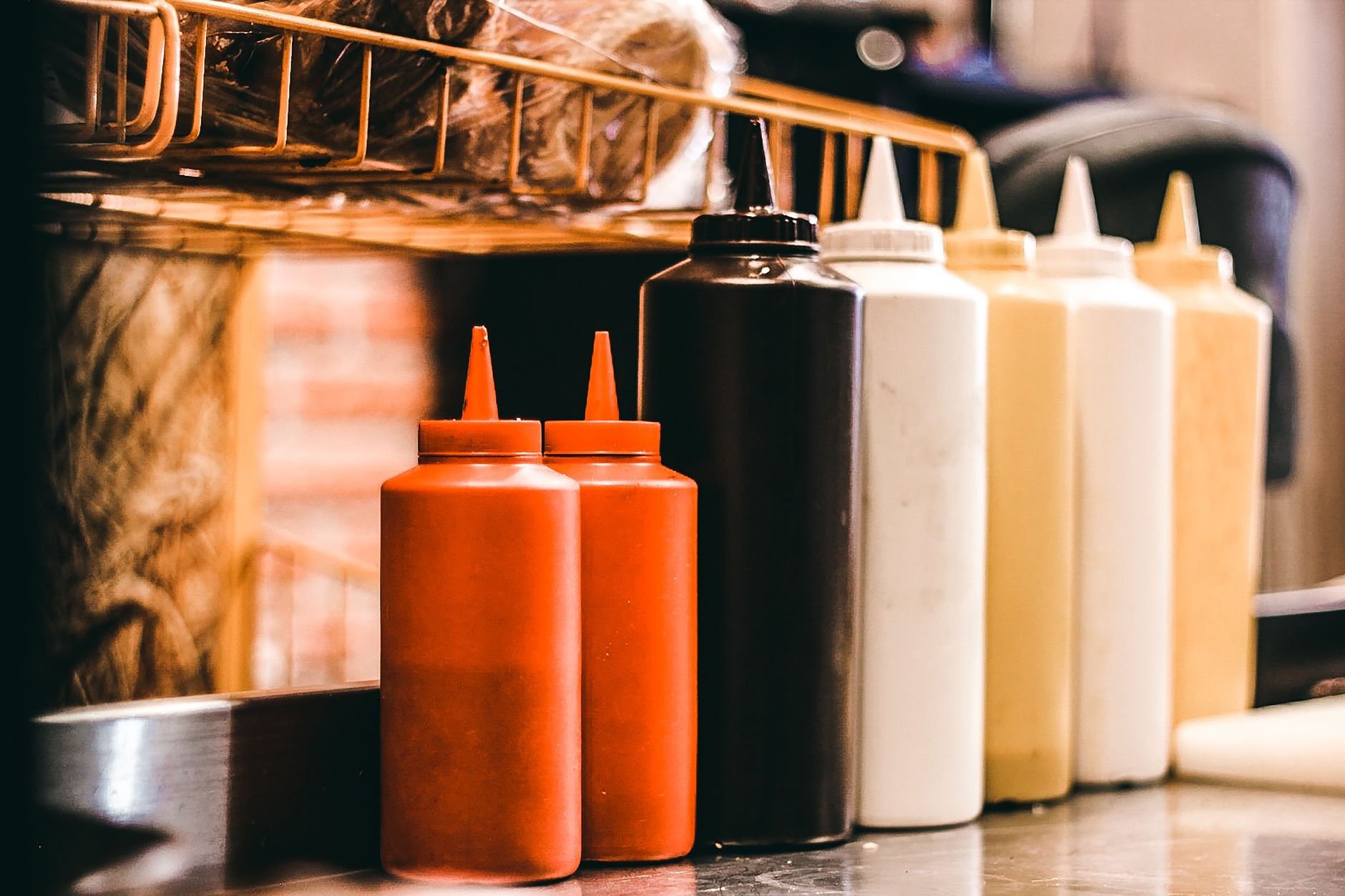 Vibrant condiment bottles lined up in a restaurant kitchen, showcasing various sauces.